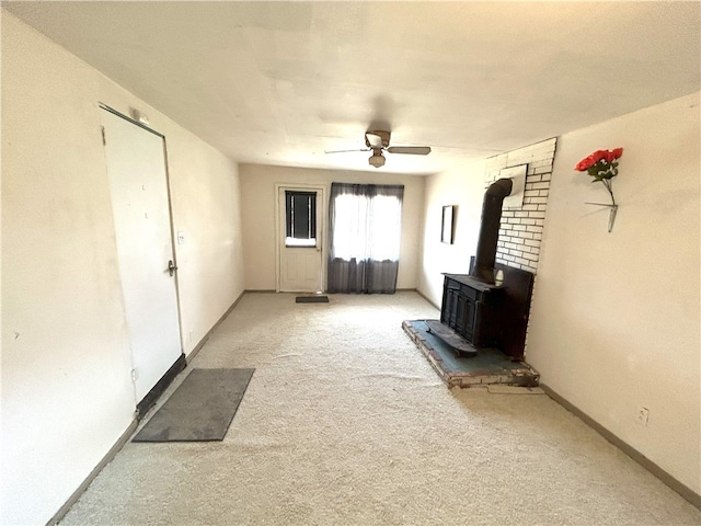 unfurnished living room with ceiling fan, light carpet, and a wood stove