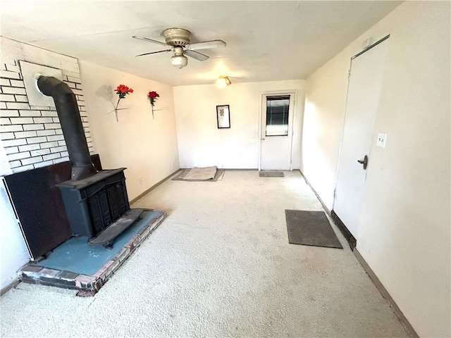 unfurnished living room featuring a wood stove, carpet floors, and ceiling fan