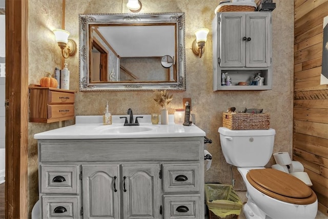 bathroom featuring toilet, vanity, and wooden walls