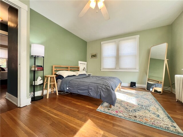 bedroom with dark hardwood / wood-style flooring, multiple windows, radiator, and ceiling fan