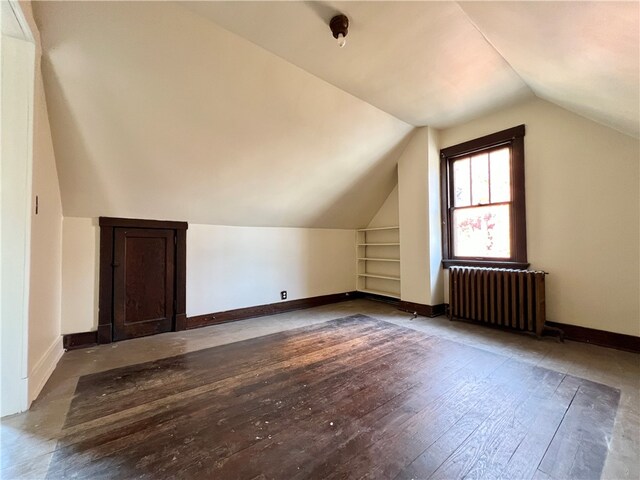 additional living space featuring radiator heating unit, dark wood-type flooring, built in features, and vaulted ceiling