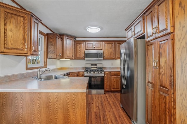 kitchen with kitchen peninsula, appliances with stainless steel finishes, a textured ceiling, light hardwood / wood-style floors, and sink