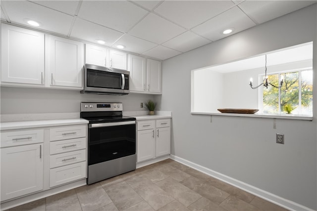 kitchen with appliances with stainless steel finishes, a drop ceiling, decorative light fixtures, white cabinets, and a notable chandelier