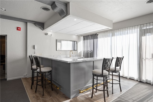 kitchen featuring light hardwood / wood-style flooring, kitchen peninsula, a textured ceiling, and a kitchen bar