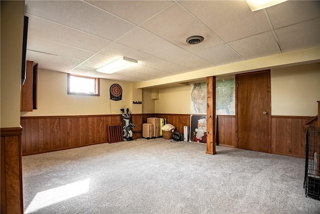 basement with carpet floors, a paneled ceiling, and wood walls