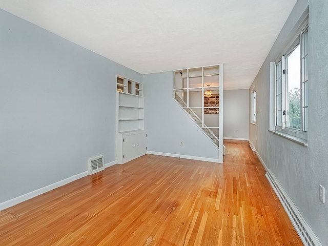 unfurnished room with light hardwood / wood-style flooring, baseboard heating, and built in shelves