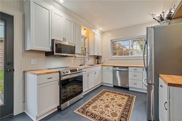 kitchen with sink, butcher block counters, stainless steel appliances, and white cabinetry