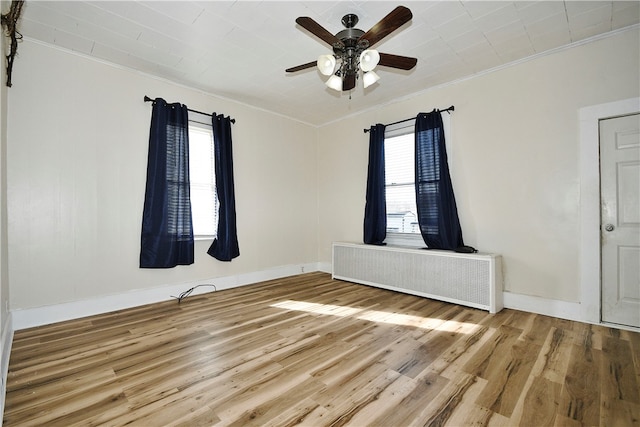 unfurnished room featuring a wealth of natural light, crown molding, radiator heating unit, and wood-type flooring