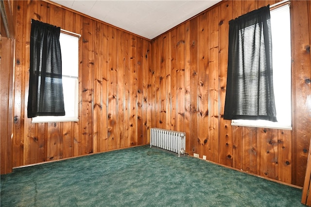 spare room with ornamental molding, radiator heating unit, wooden walls, and dark colored carpet