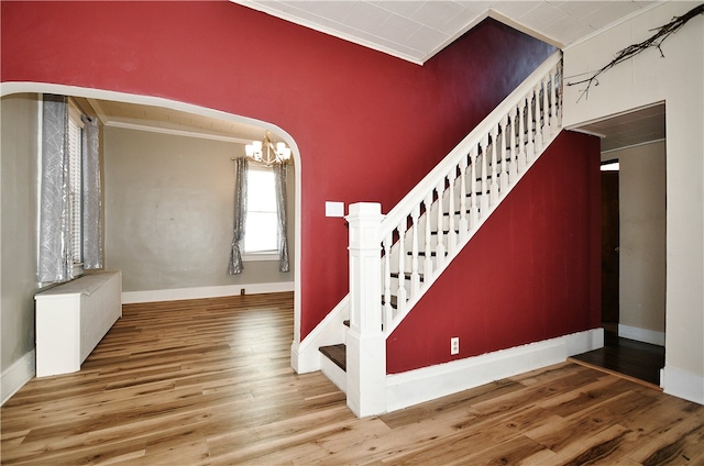 stairs with crown molding, hardwood / wood-style flooring, and an inviting chandelier