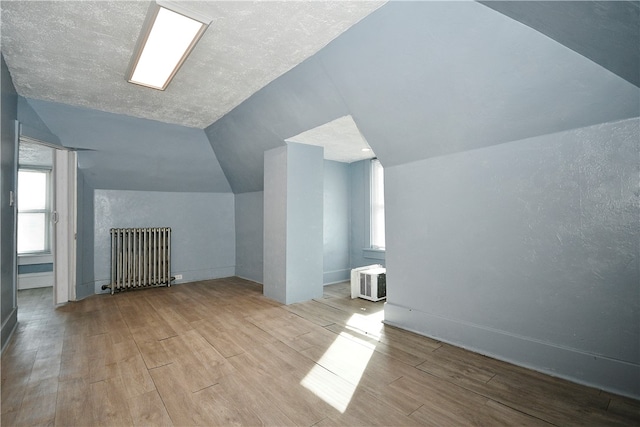 bonus room featuring radiator, vaulted ceiling, light wood-type flooring, and plenty of natural light