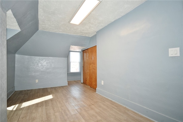 additional living space with vaulted ceiling, a textured ceiling, and light hardwood / wood-style flooring