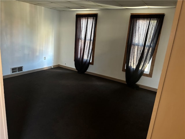 carpeted empty room featuring a wealth of natural light and a drop ceiling