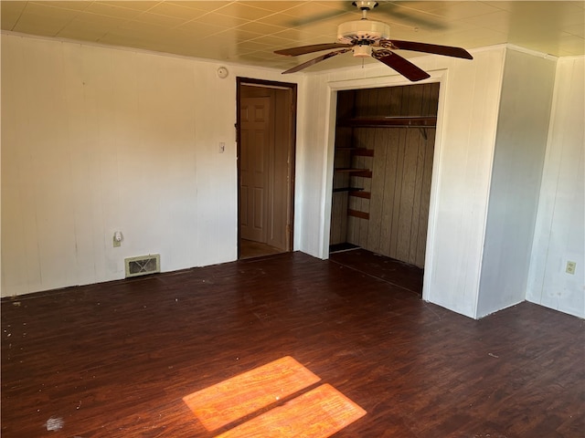 unfurnished room featuring wood walls, dark hardwood / wood-style floors, and ceiling fan