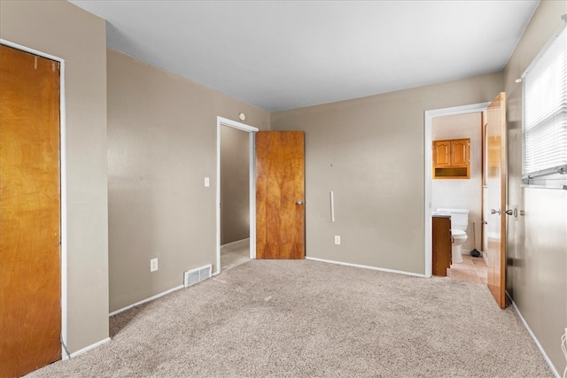 unfurnished bedroom with a closet, ensuite bath, and light colored carpet