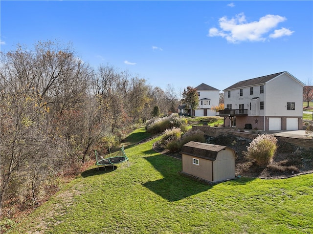 view of yard featuring a wooden deck, a storage unit, a garage, and a trampoline