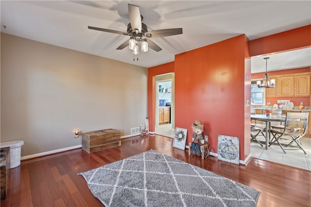 living area with ceiling fan with notable chandelier and dark wood-type flooring