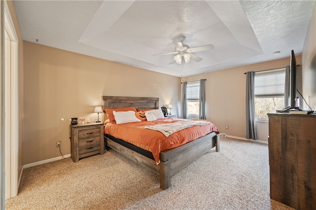 carpeted bedroom with a textured ceiling, a raised ceiling, multiple windows, and ceiling fan