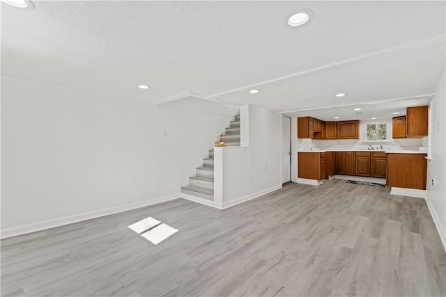 unfurnished living room featuring sink, light hardwood / wood-style flooring, and a textured ceiling