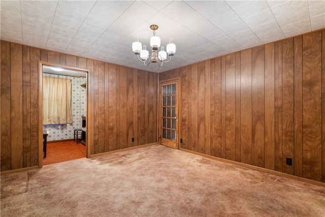 spare room with wooden walls, carpet floors, and a chandelier