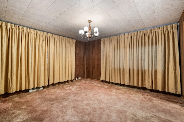 carpeted spare room featuring a notable chandelier and wood walls