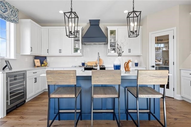 kitchen featuring custom range hood, white cabinets, a center island, and beverage cooler