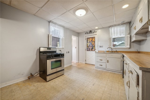 kitchen featuring gas range, a drop ceiling, white cabinets, and sink