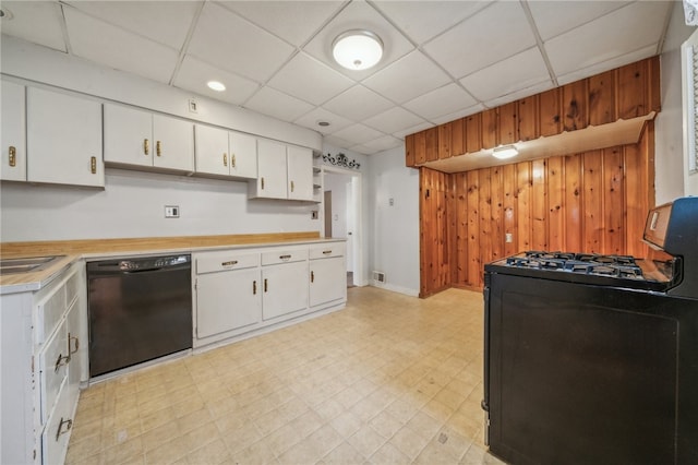 kitchen featuring a drop ceiling, white cabinets, black appliances, and wood walls