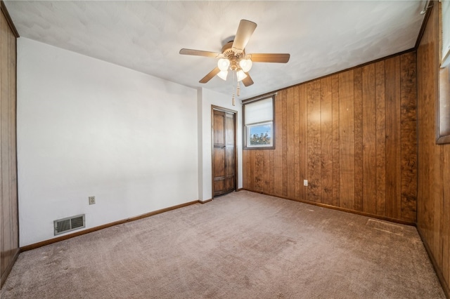 carpeted empty room featuring ceiling fan and wood walls