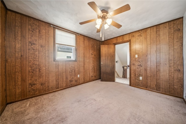 unfurnished room with wooden walls, light carpet, and ceiling fan