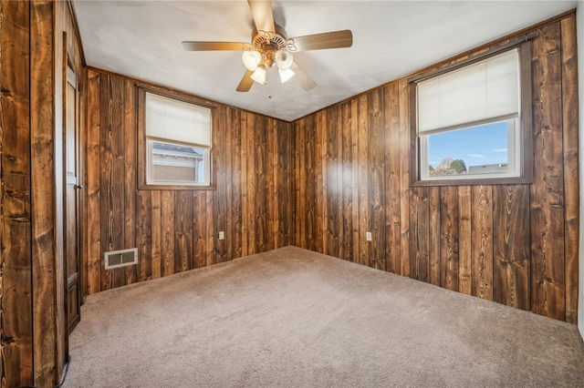 carpeted spare room featuring ceiling fan and wood walls