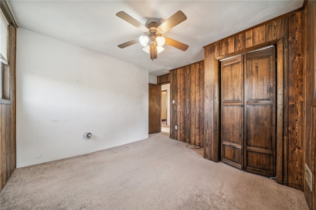 unfurnished bedroom with light carpet, a closet, wood walls, and ceiling fan