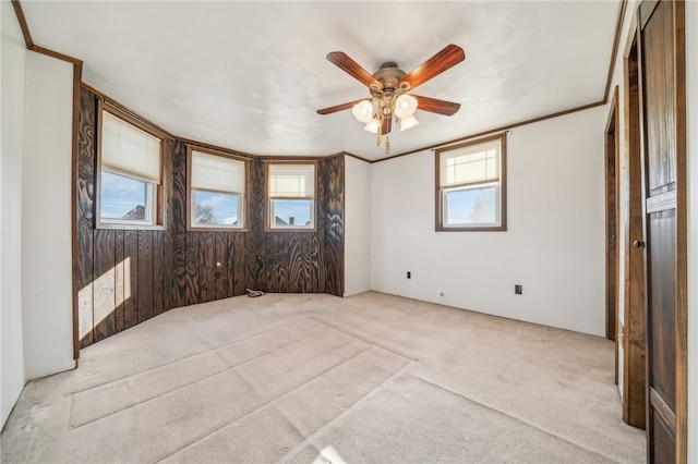 carpeted spare room with a wealth of natural light, ornamental molding, and ceiling fan