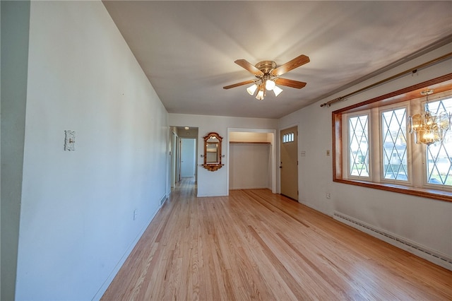 empty room with ceiling fan with notable chandelier, baseboard heating, and light hardwood / wood-style flooring