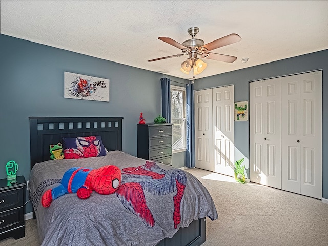 carpeted bedroom with ceiling fan, a textured ceiling, and multiple closets