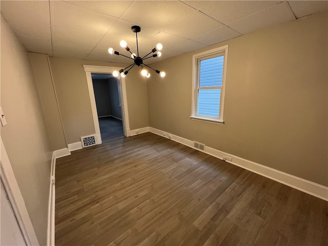 spare room with a paneled ceiling, a notable chandelier, and dark hardwood / wood-style floors