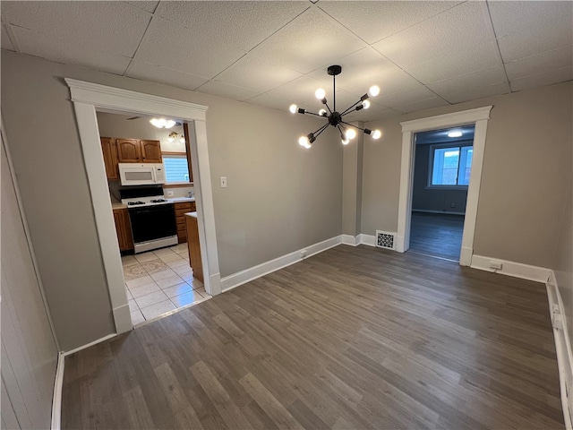 unfurnished dining area featuring a drop ceiling, a chandelier, and light wood-type flooring