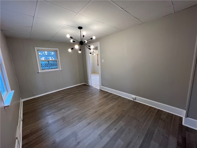 spare room featuring an inviting chandelier, dark hardwood / wood-style flooring, and a drop ceiling