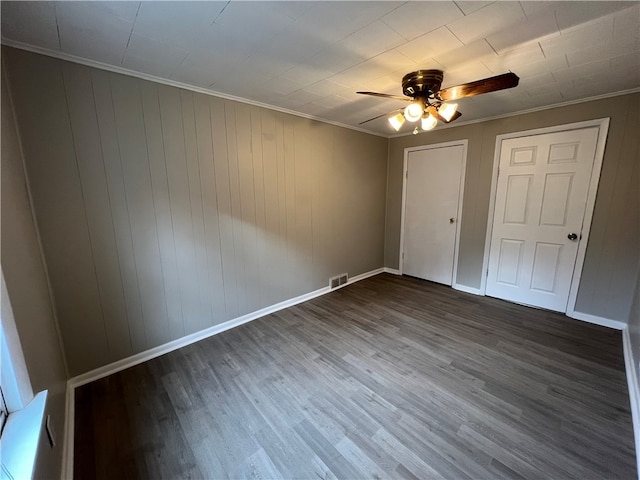 unfurnished bedroom with dark hardwood / wood-style flooring, ornamental molding, wooden walls, and ceiling fan