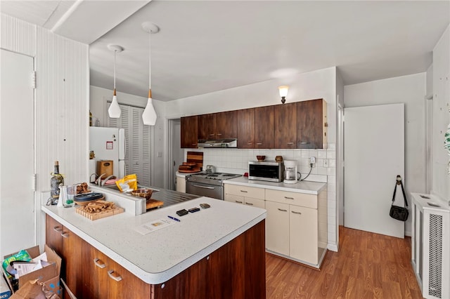 kitchen with exhaust hood, backsplash, appliances with stainless steel finishes, light hardwood / wood-style flooring, and decorative light fixtures