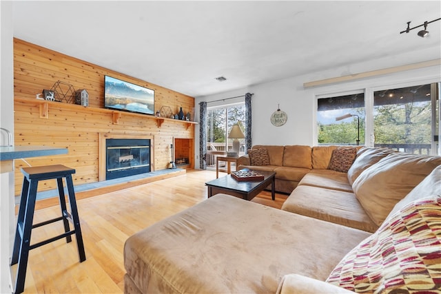 living room with rail lighting, wood walls, and light hardwood / wood-style flooring