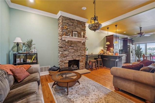 living room with light wood-type flooring, visible vents, crown molding, and a stone fireplace