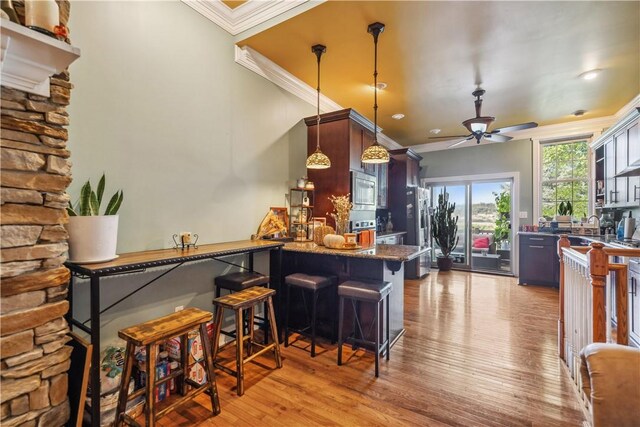 kitchen featuring a kitchen breakfast bar, appliances with stainless steel finishes, ceiling fan, crown molding, and light hardwood / wood-style flooring