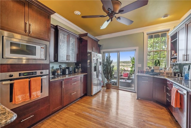 kitchen with stainless steel appliances, dark stone countertops, light wood-style flooring, and crown molding