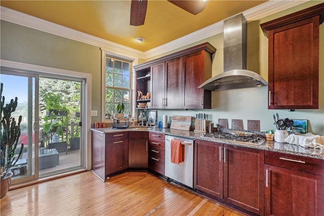 kitchen with appliances with stainless steel finishes, reddish brown cabinets, light wood-style floors, and wall chimney exhaust hood