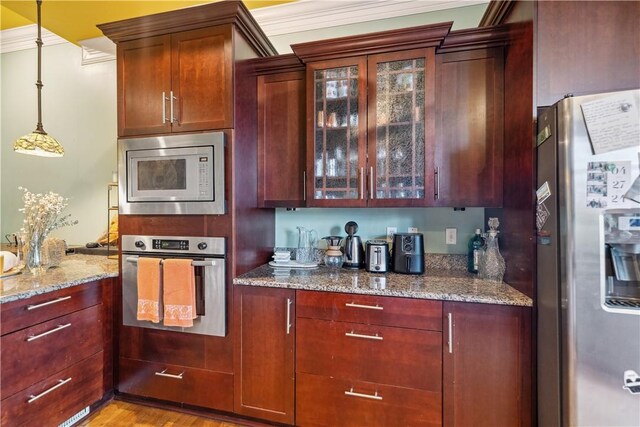 kitchen featuring light stone countertops, pendant lighting, light wood-type flooring, appliances with stainless steel finishes, and ornamental molding