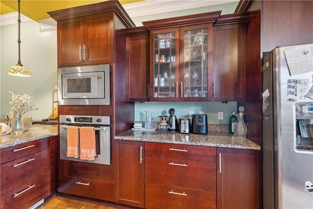 kitchen featuring light wood finished floors, appliances with stainless steel finishes, glass insert cabinets, hanging light fixtures, and light stone countertops