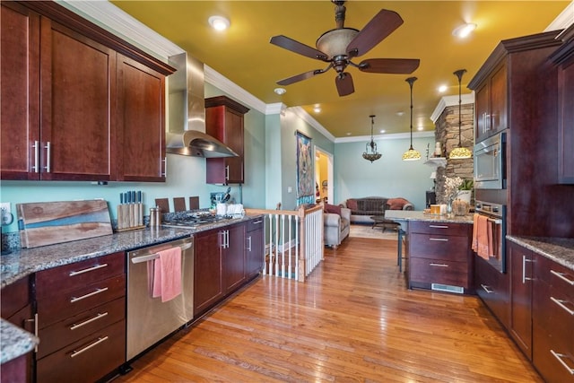 kitchen with stainless steel appliances, hanging light fixtures, light wood-style flooring, dark stone countertops, and wall chimney exhaust hood