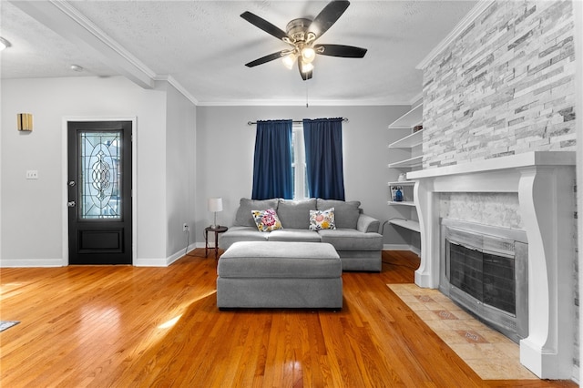 living room with a stone fireplace, light hardwood / wood-style flooring, ornamental molding, a textured ceiling, and ceiling fan