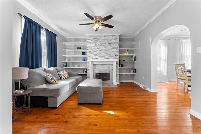 living room featuring ornamental molding, wood-type flooring, a fireplace, and ceiling fan